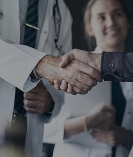 Two doctors shaking hands in front of a smiling patient.